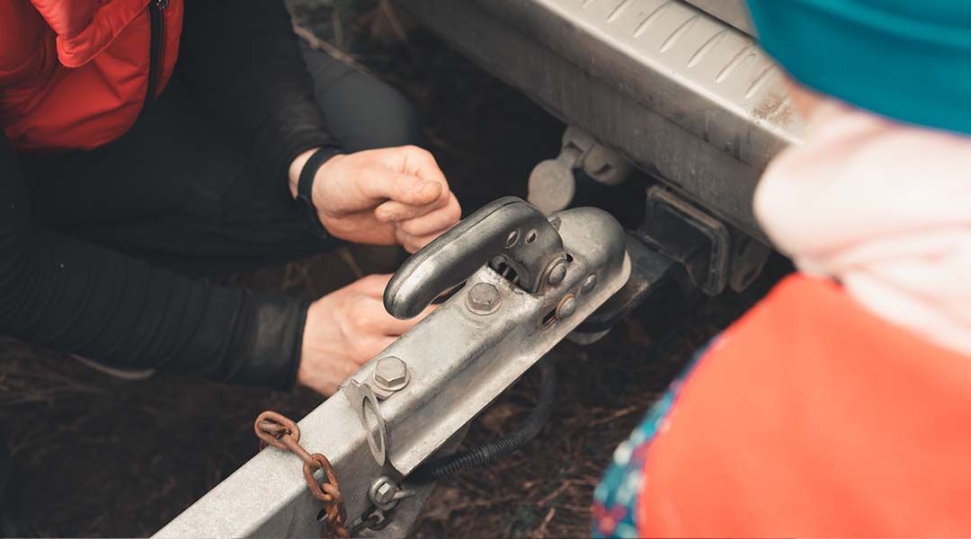 A person is attaching a trailer to a car.