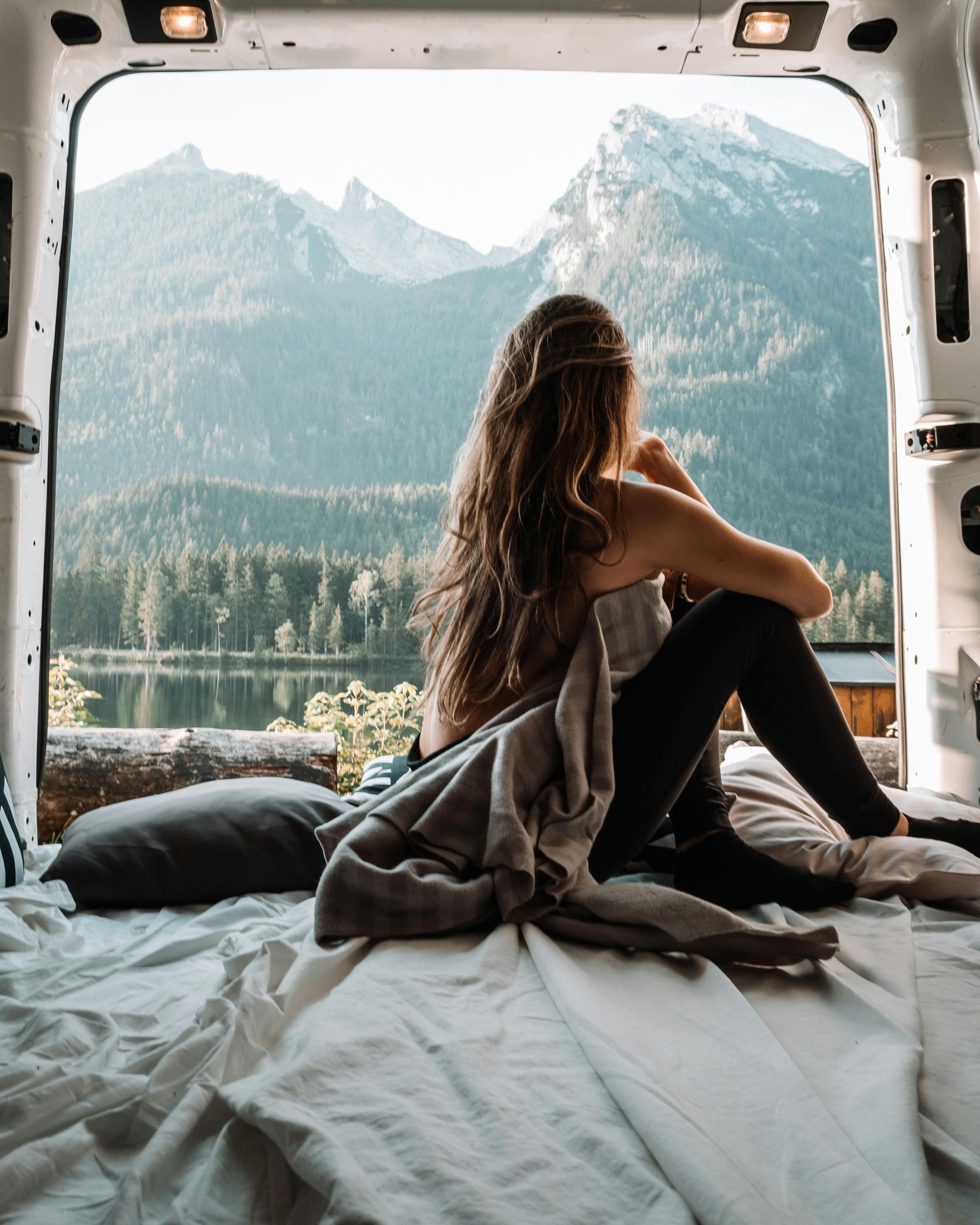 A woman is sitting in the back of a van looking out the window.