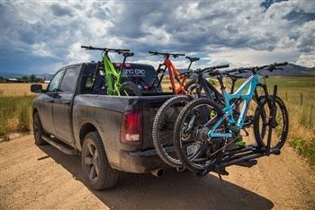 A truck with bikes in the back of it is parked on a dirt road.