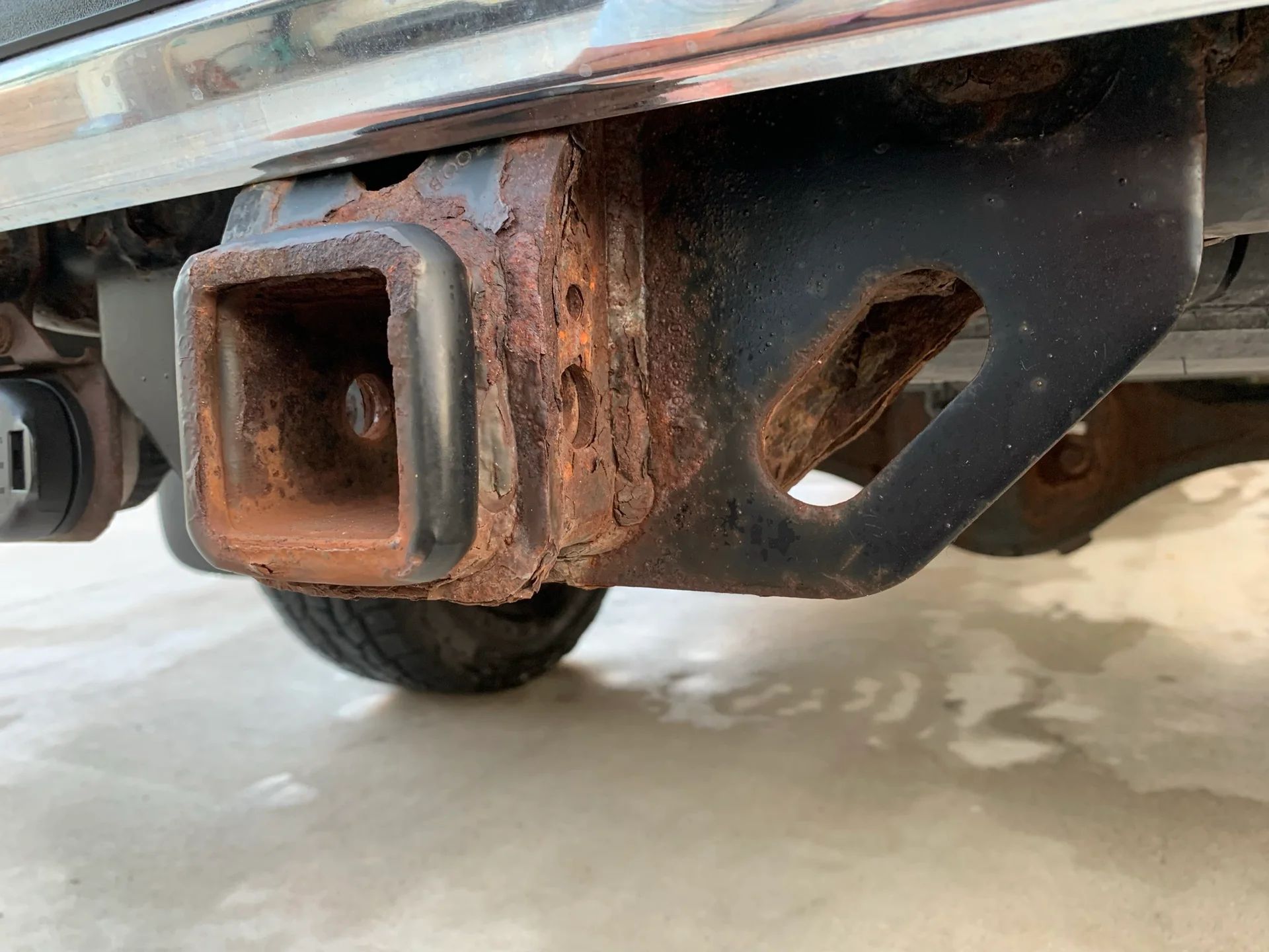 A close up of a rusty hitch on a car.