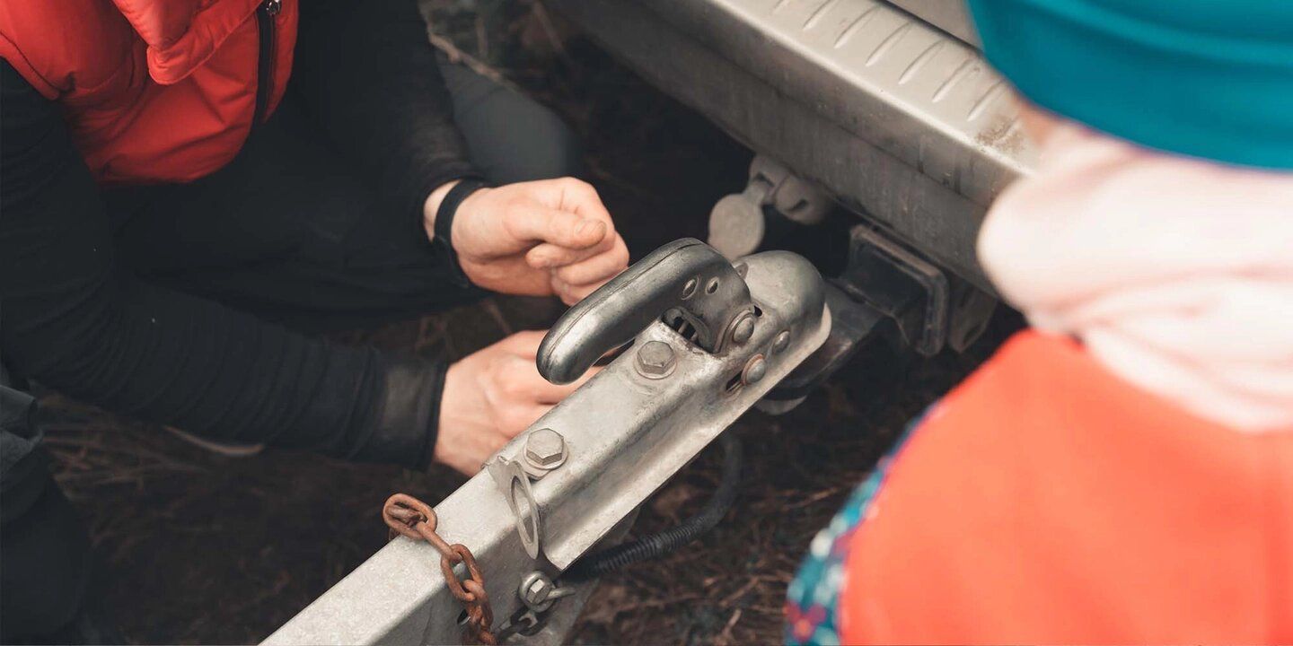 A man and a child are attaching a trailer to a car.