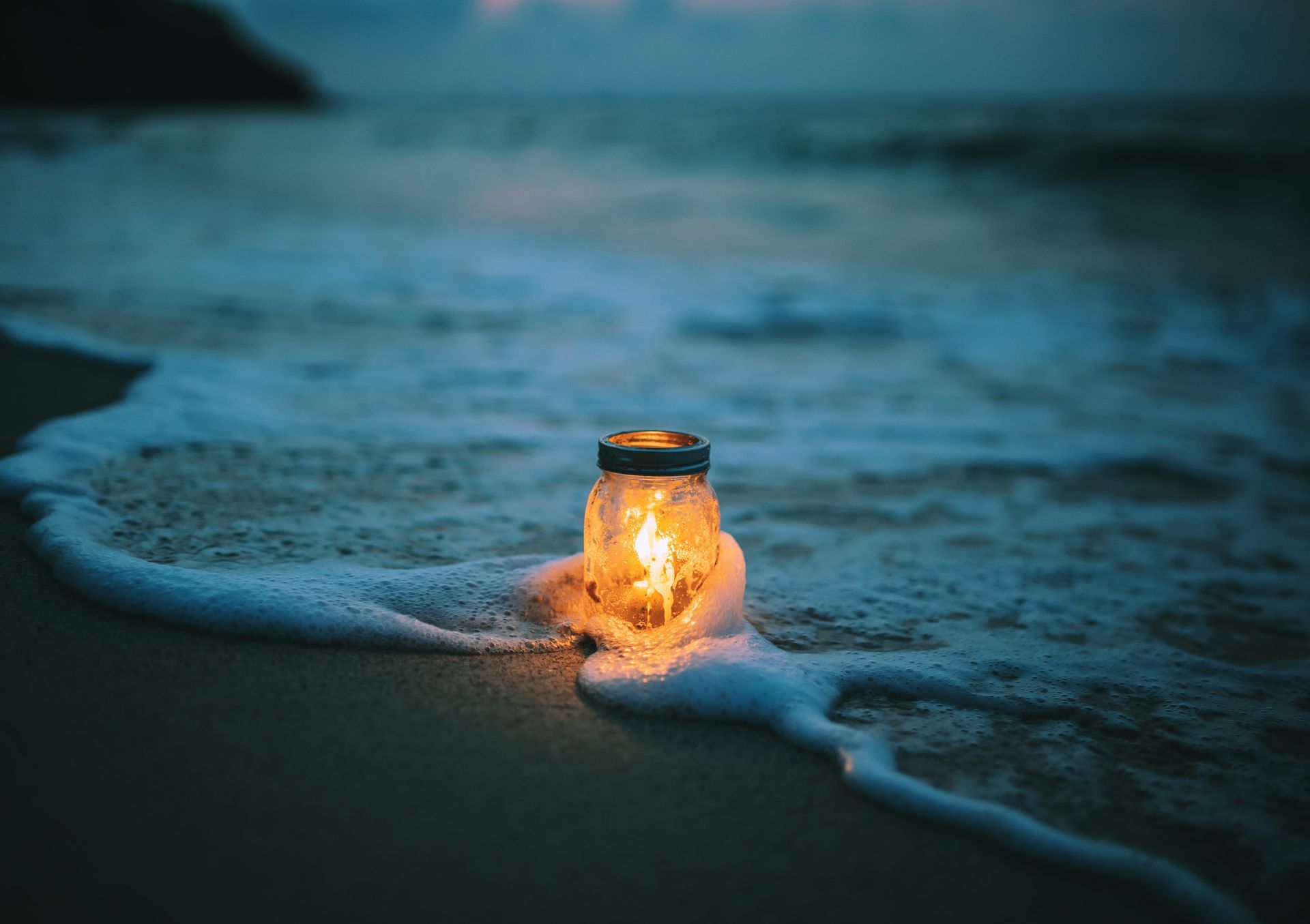 Glowing jar lantern on a dark beach, surrounded by foamy waves at dusk