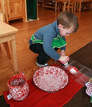 A little boy with an apron on is working montessori like