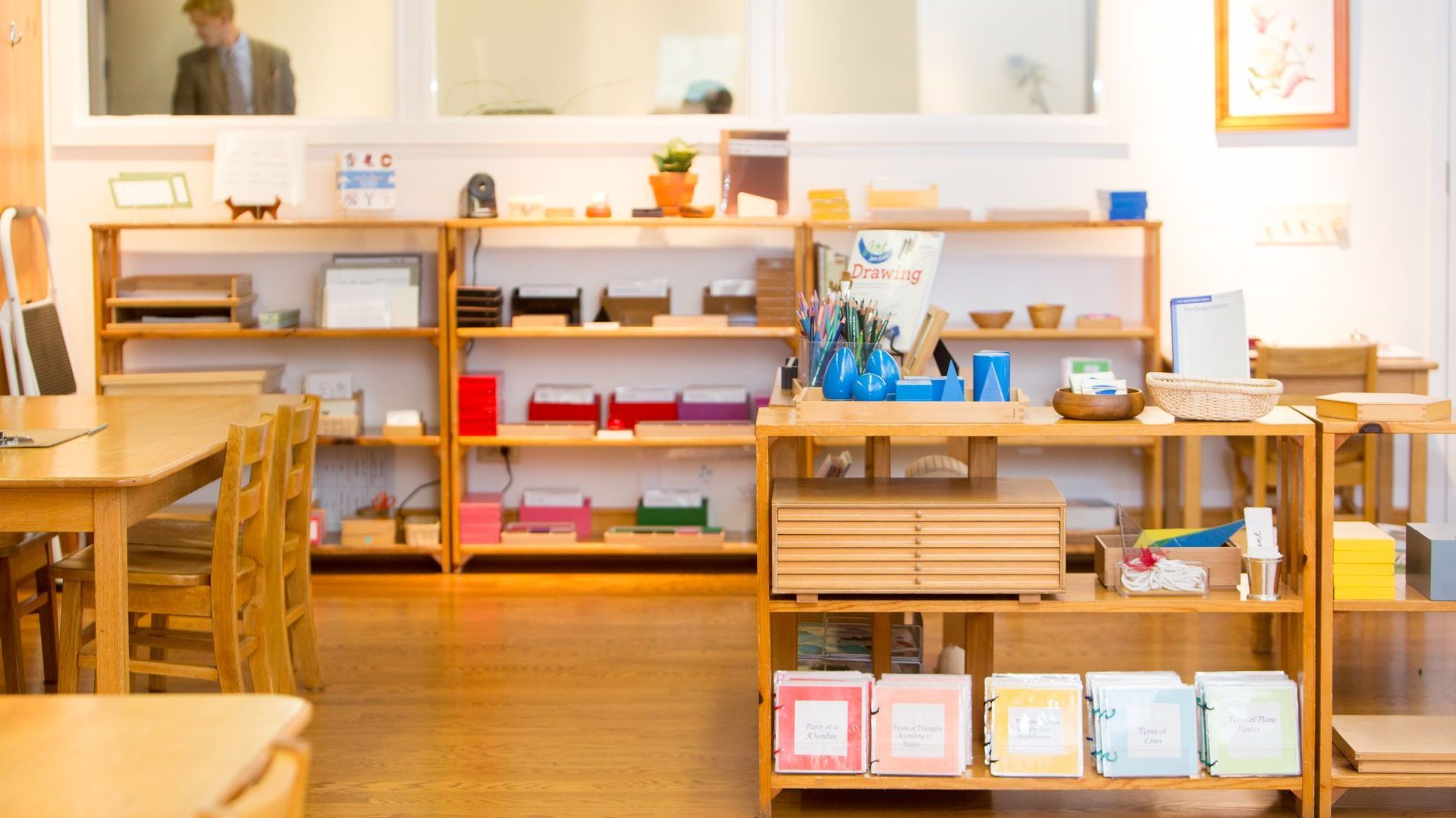 A Montessori classroom filled with wooden shelves and tables and chairs.