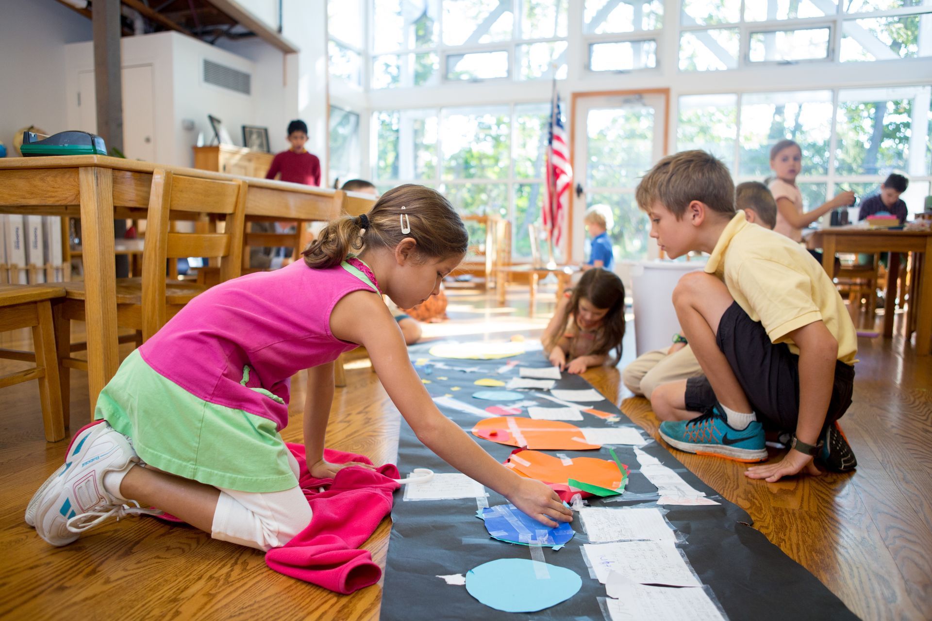A group of Montessori children are working on the floor in a classroom.