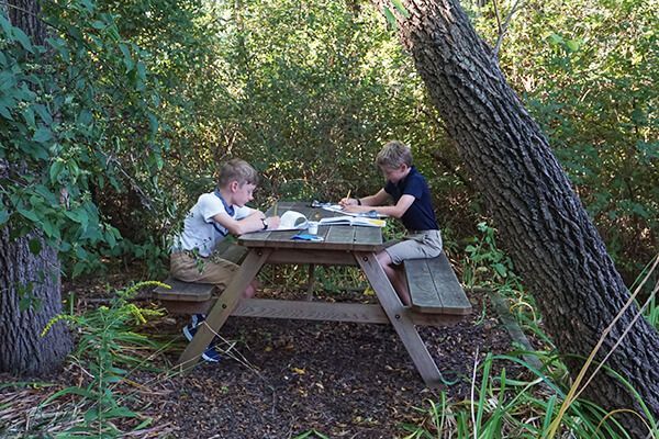 Two young boys are sitting at a picnic table in the woods.