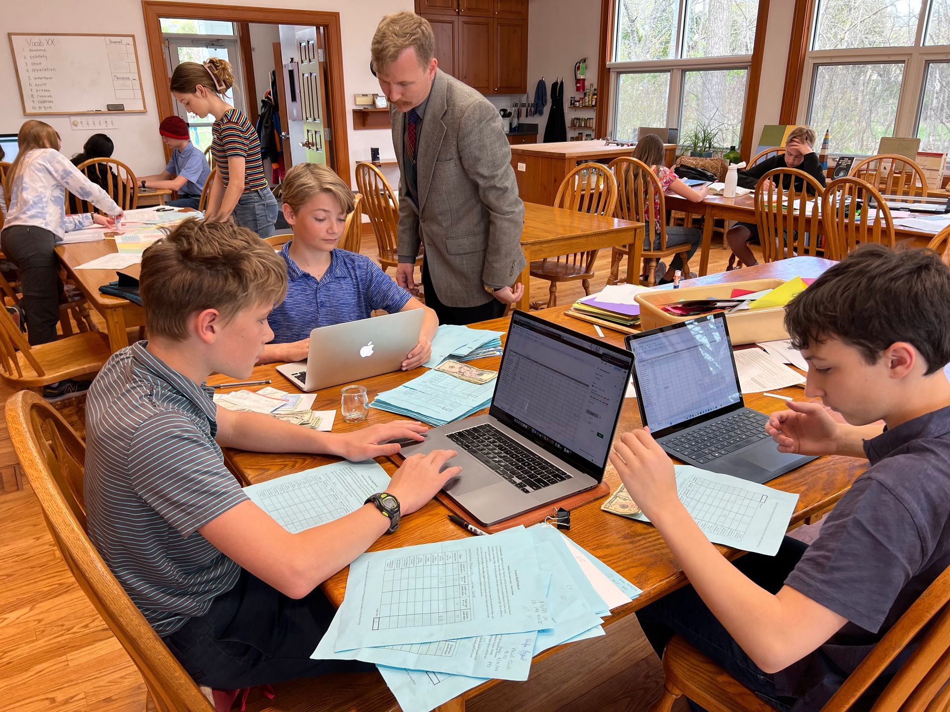 Montessori children are sitting at a table with laptops.