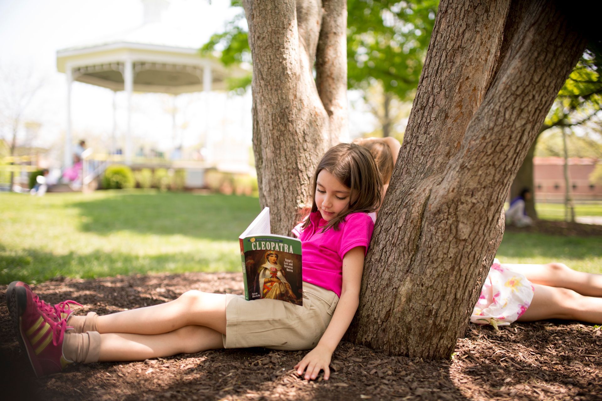 A Montessori child is sitting under a tree reading a book.