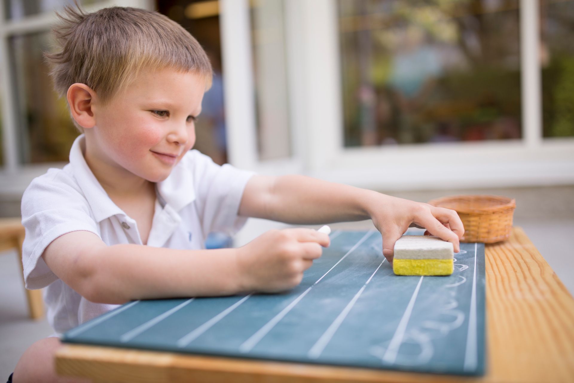 A Montessori child is sitting at a table working with a chalkboard.
