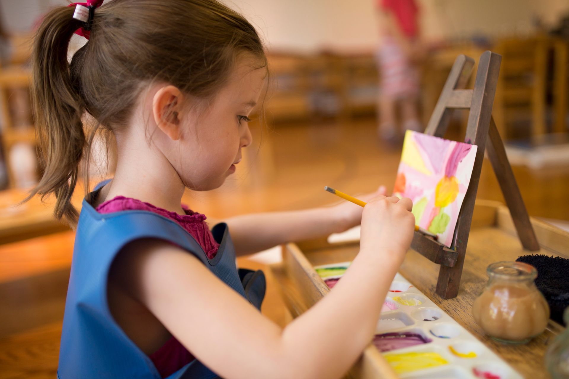 A Montessori child is painting a picture on an easel.