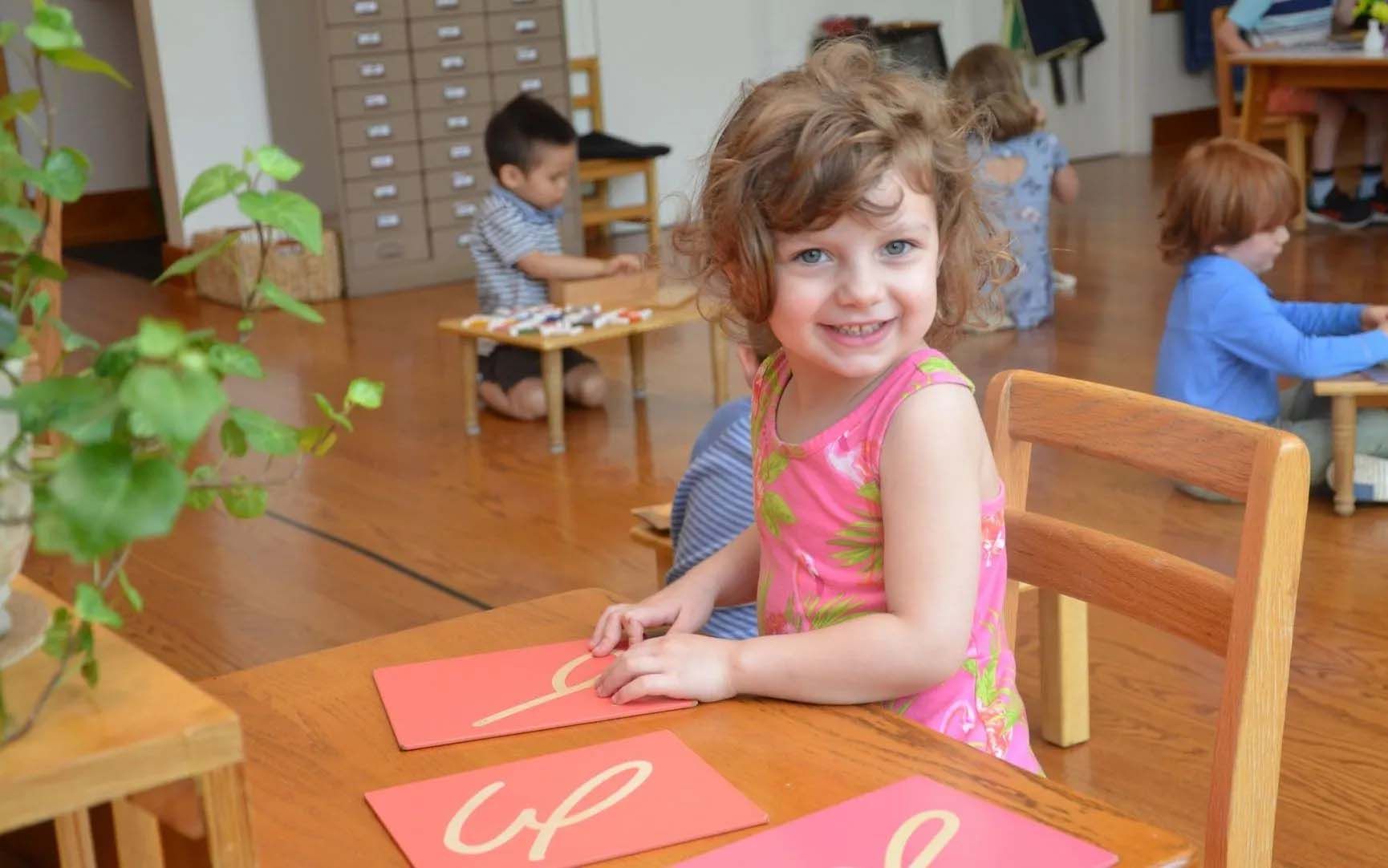 Montessori child is sitting at a table writing on a piece of paper