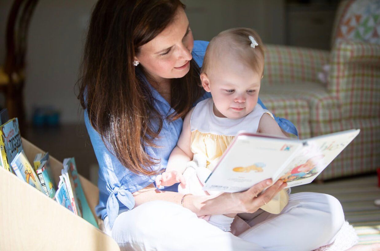 A mother reads a book aloud to a baby on her lap