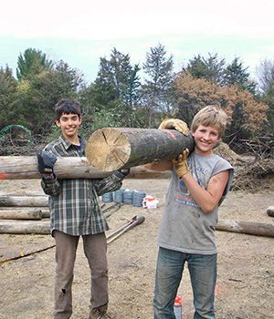 Two adolescents hlding big wood logs and smiling to the camara