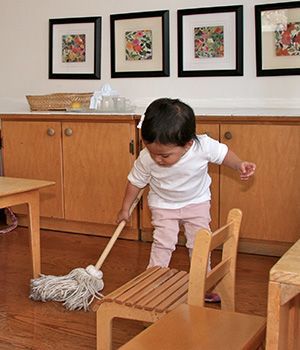 A little girl cleaning the floor with a small mop in a Montessori classroom