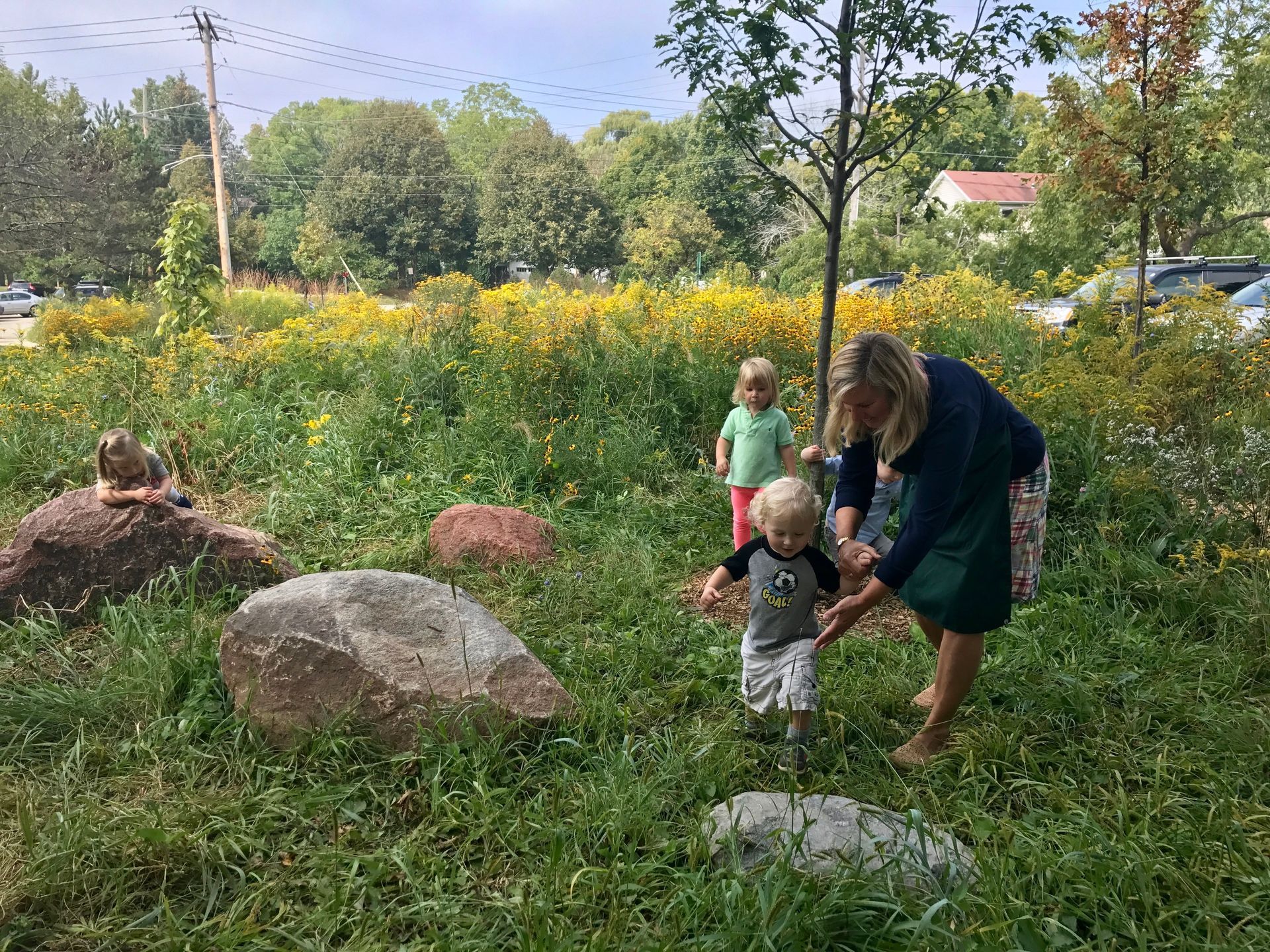 A guide and two Montessori children are walking through a grassy field.