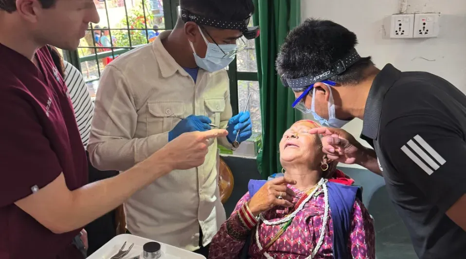 A group of men are examining a woman 's eyes in a dental office.