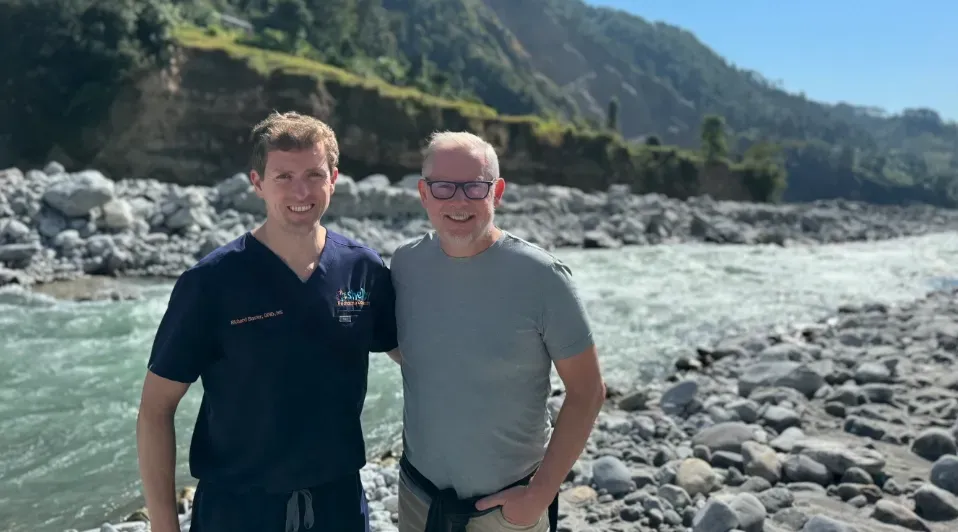 Two men are posing for a picture in front of a river.