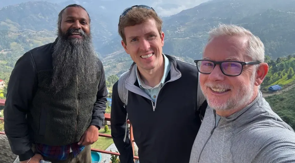 Three men are posing for a selfie in front of a mountain.