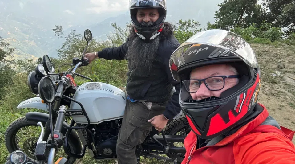 Two men wearing helmets are standing next to a motorcycle.