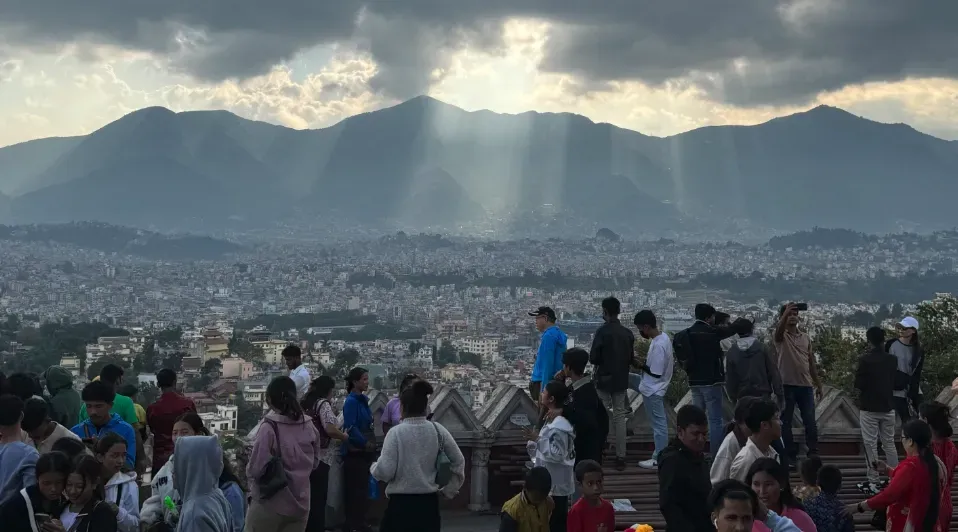 A large group of people are standing on top of a hill overlooking a city.