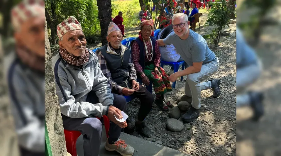 A man is kneeling down next to a group of elderly people sitting on red stools.