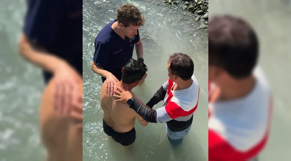 A man is being baptised in a river by two other men.