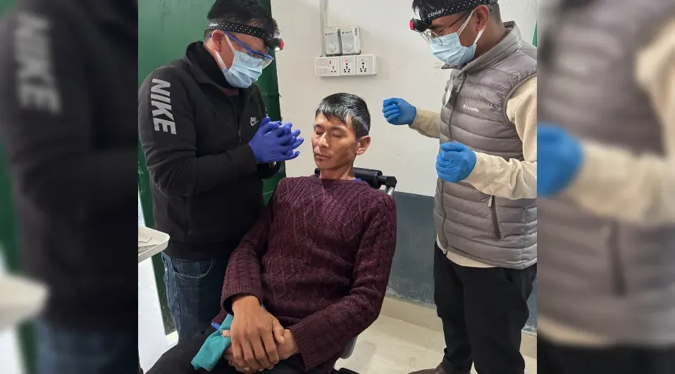 A man in a wheelchair is being examined by two men wearing masks and gloves.