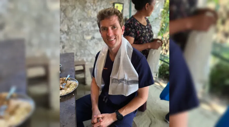 A man in scrubs is sitting with a towel around his neck.