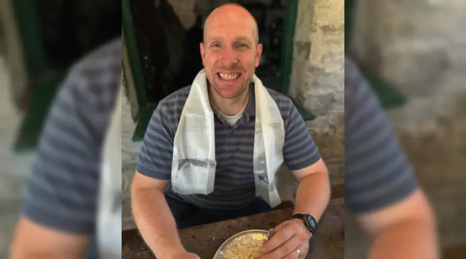 A man with a towel around his neck is sitting at a table with a bowl of food.