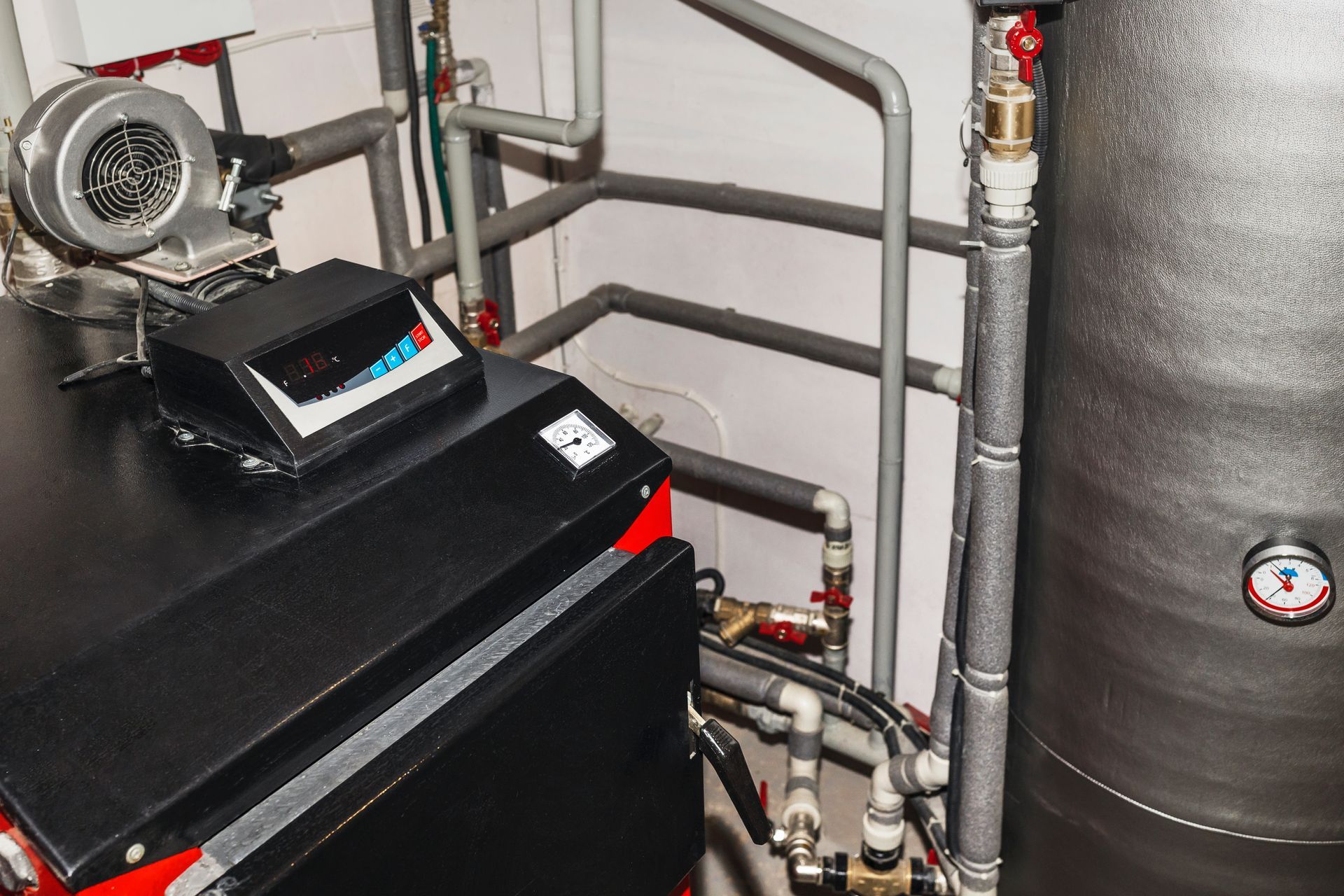 Boiler room with black heating unit, pipes, vent fan, and large insulated tank