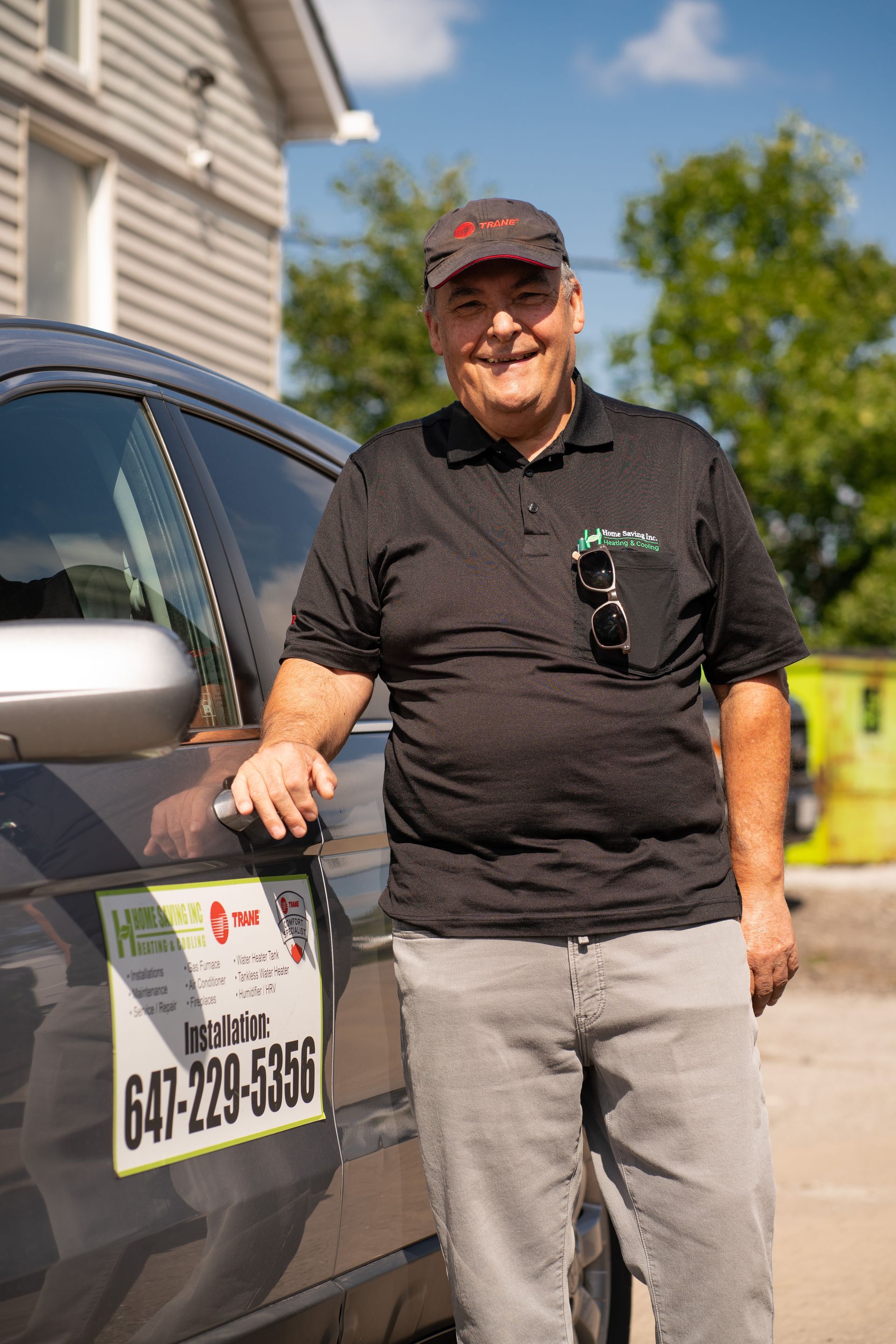Smiling person stands beside a black truck with a phone number on the door in a driveway.