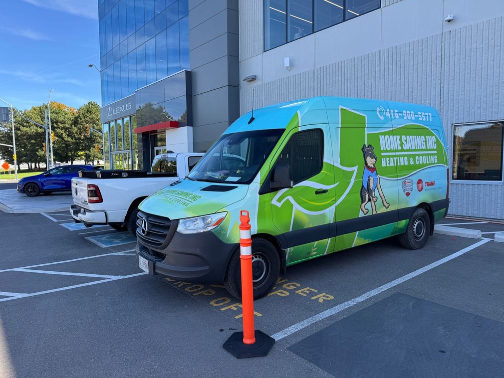 Green delivery van parked in a lot beside a white pickup and office building under clear blue sky