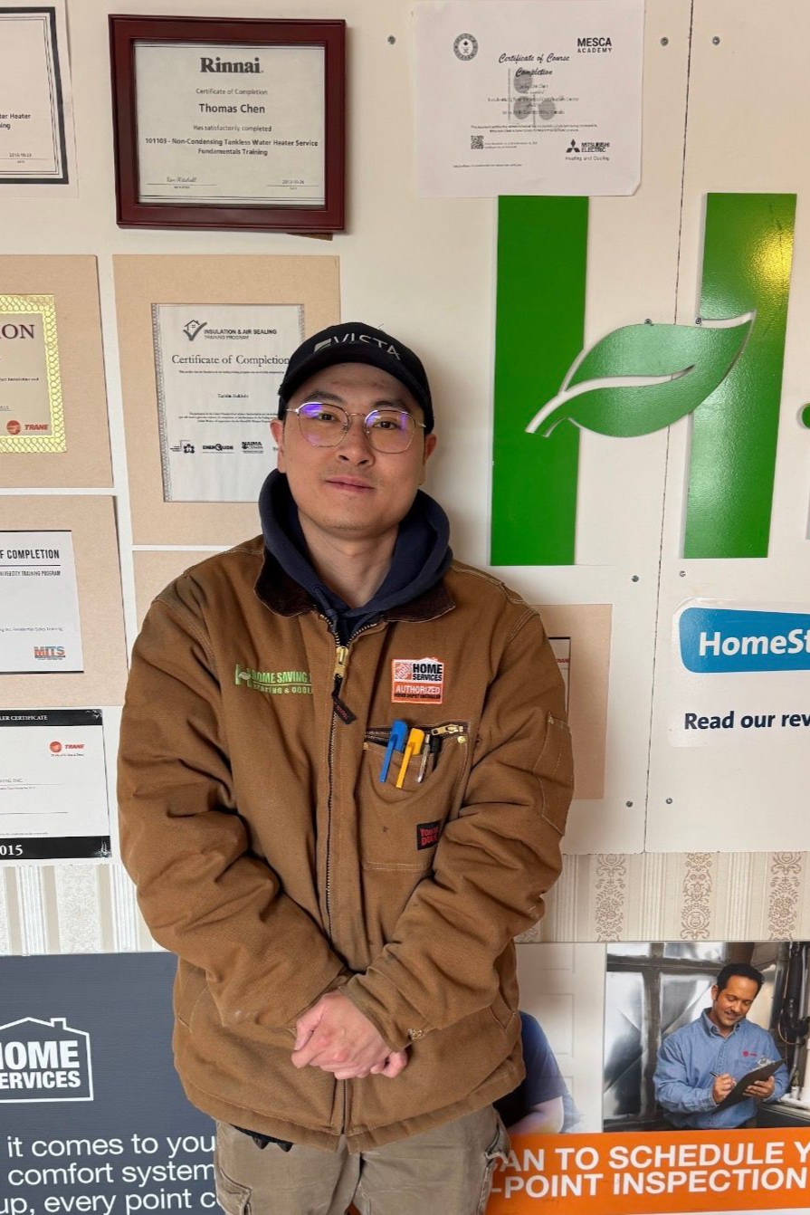 Man in brown jacket and cap standing indoors in front of framed certificates and green leaf logo.
