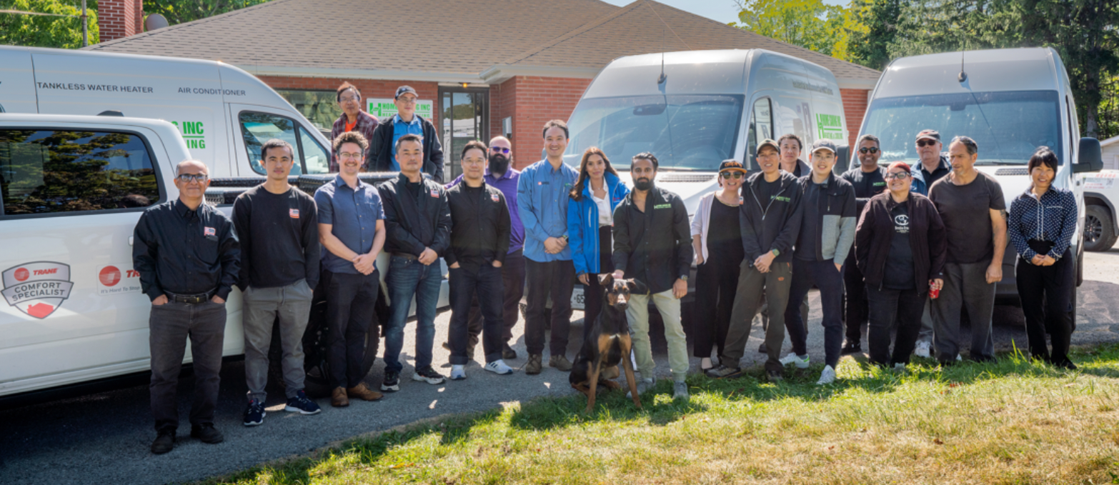 Group of people standing in front of three white vans on a grassy lot, posing for a photo