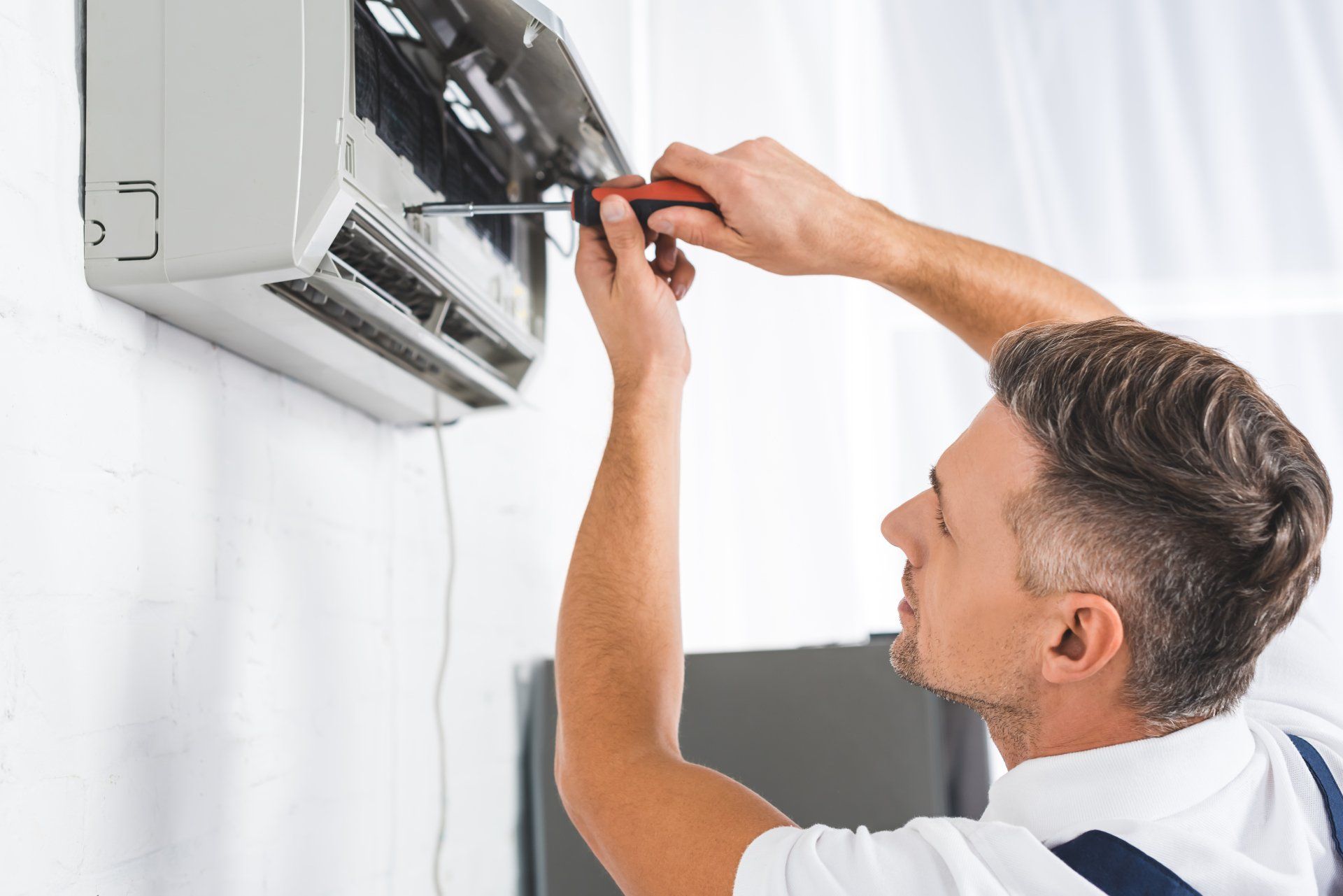 contractor repairing an Air Conditioning unit with a screwdriver