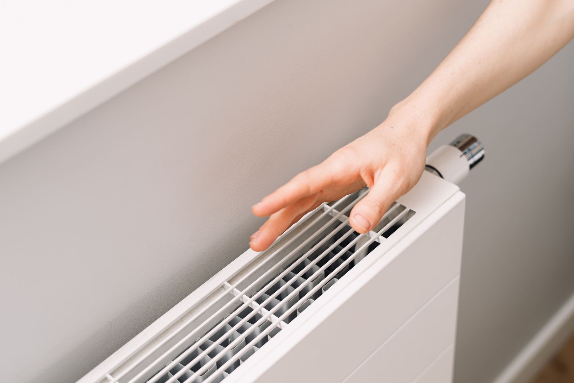 Hand touching a white radiator thermostat in a home interior