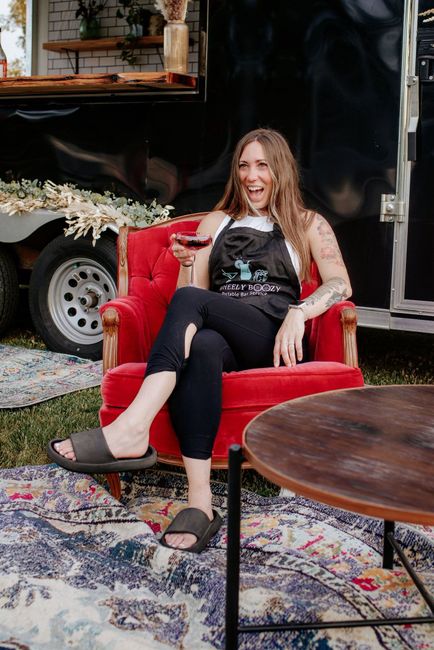 Woman sitting on a red armchair beside a round wooden table in an outdoor lounge area.
