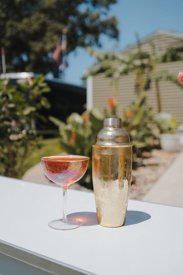 Two cocktails on a white table outdoors in bright sunlight, with a blurred patio garden background