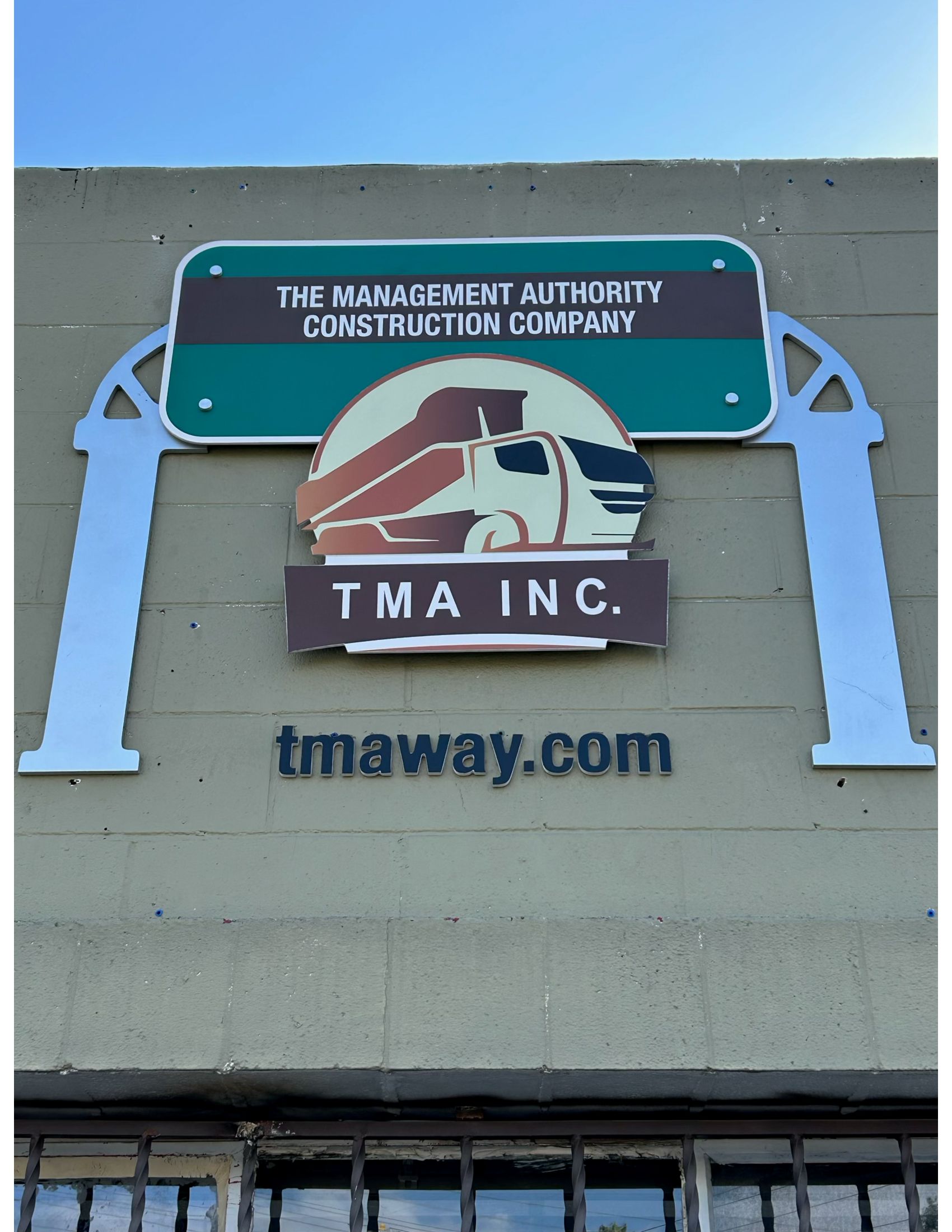 Sign for TMA Inc. construction company: green and brown logo, white truck graphic, website address tmaway.com.