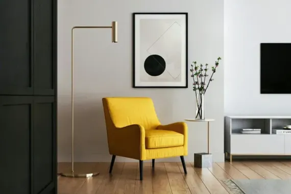 Modern living room with a yellow chair, floor lamp, framed wall art, and TV console