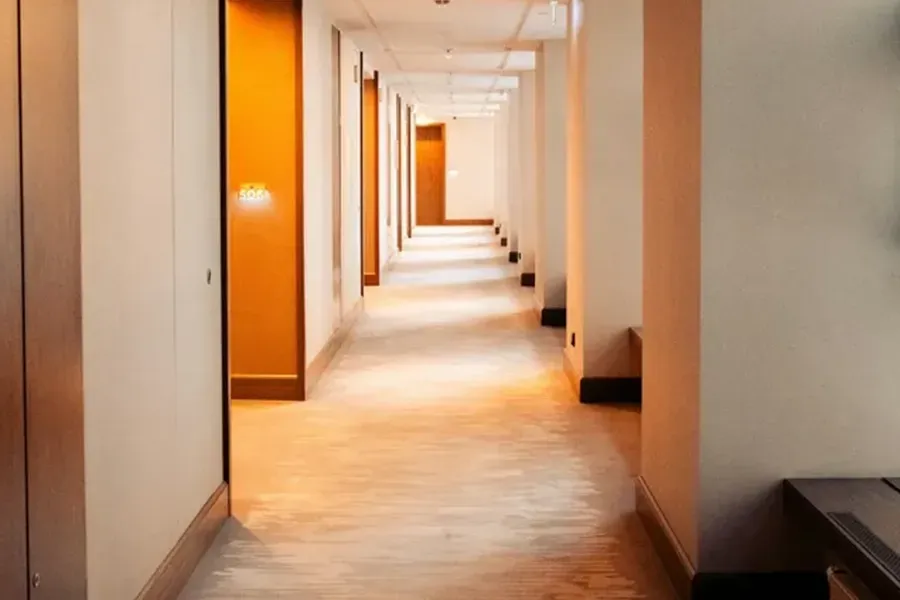 Long, empty hallway with orange doors and beige walls, lit by soft natural light