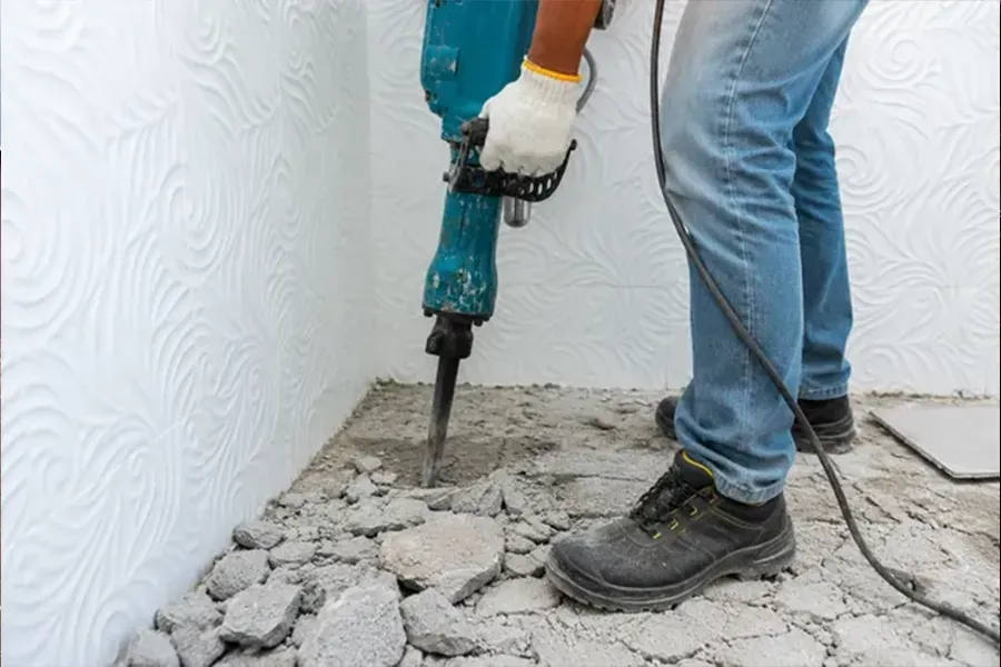 Person using a jackhammer to break up concrete floor indoors