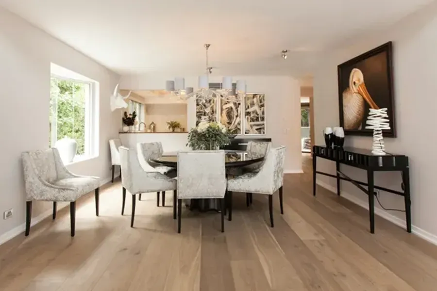 Bright dining room with a white table, upholstered chairs, chandelier, and black console against beige walls.