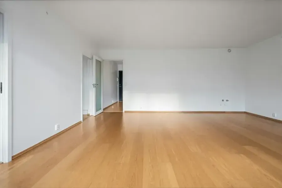 Empty unfurnished room with light wood floor, white walls, and large windows.