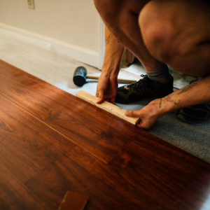 Person installing a hardwood floor seam with a measuring tape and drill nearby