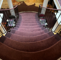 Curved carpeted staircase with dark railings and white columns in a warm-lit interior