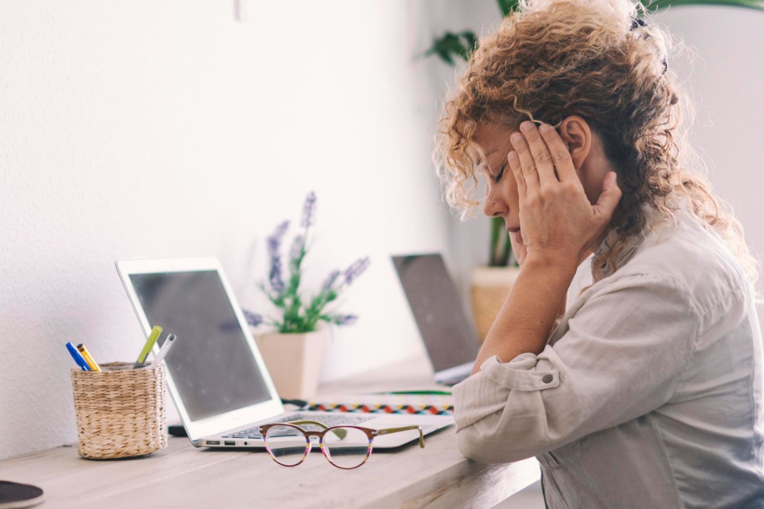 A woman is sitting at a desk with her head in her hands.
