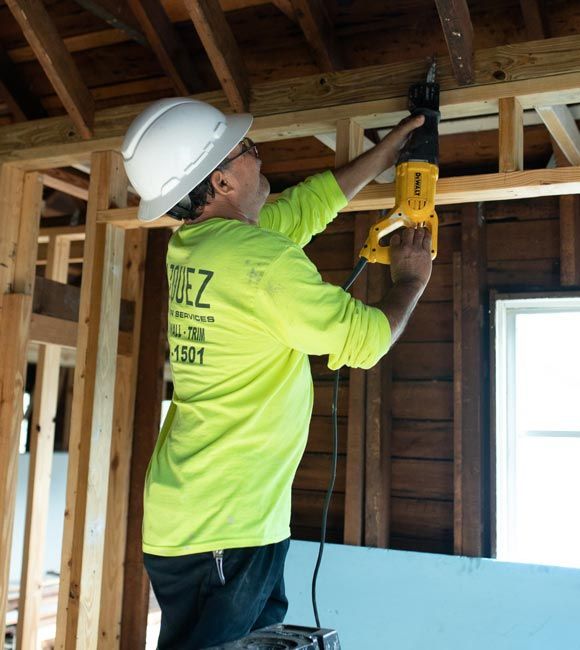 Construction worker in white hard hat using a power drill on wooden wall framing indoors