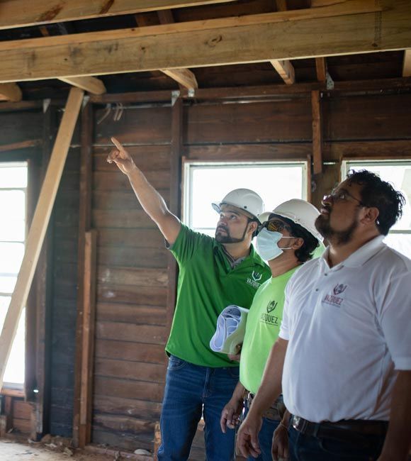Three people in hard hats inspect wooden beams inside a partially built structure