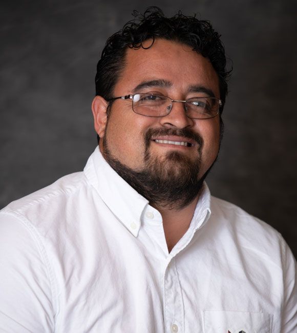 Smiling man in glasses and white shirt against a dark studio backdrop